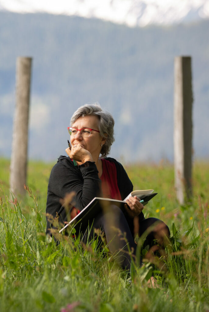 Alexandra Peischer, nachdenklich im Gras sitzend und schreibend
