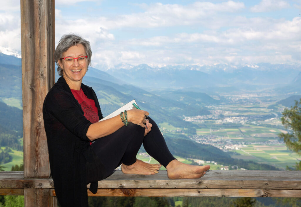 Alexandra, auf einem Holzgeländer sitzend, mit Buch und Stift in der Hand