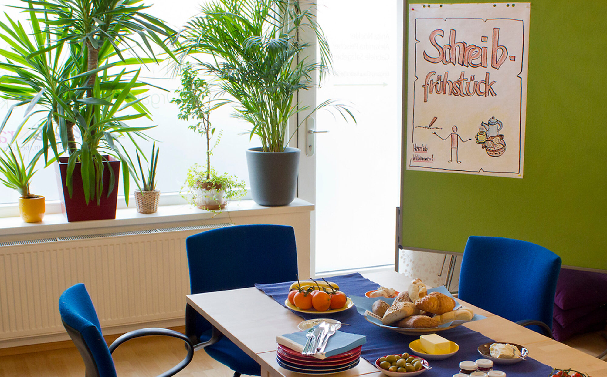 Tisch mit Brotkorb und einigen Tellern, dahinter ein Plakat "Schreibfrühstück"