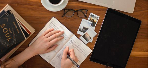 Offenes-Tagebuch-auf-Tisch-mit-Kaffeetassse-und-Brille-Hand-schreibt-Tisch