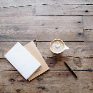 Schreibhefte auf Holztisch, daneben eine Füllfeder und eine Tasse Kaffee