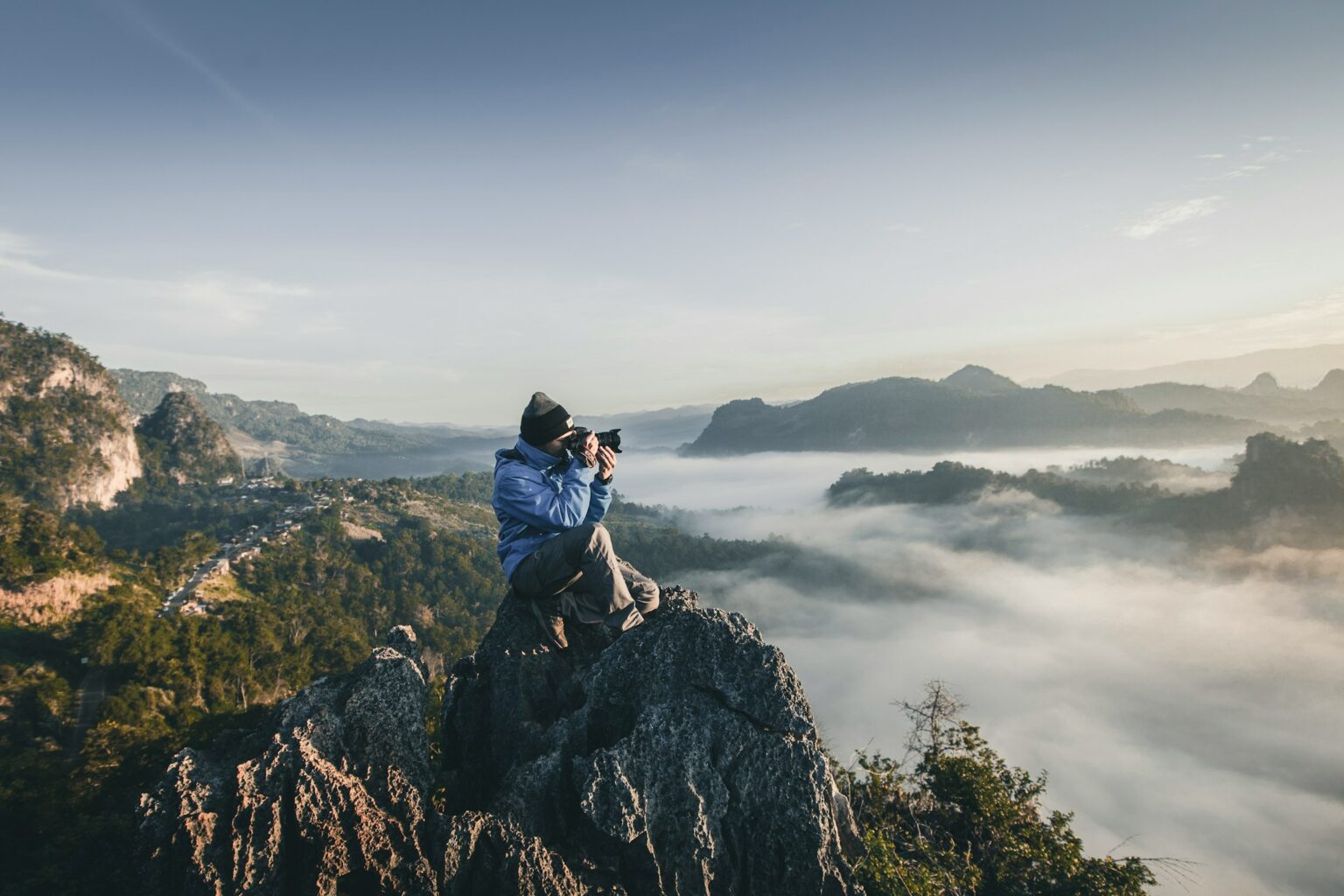 Mensch sitzt auf einem Berg und fotografiert in die Weite